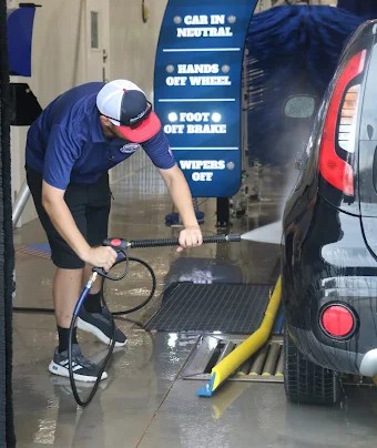 Clean Wash team member pre-rinsing a car at the tunnel entrance